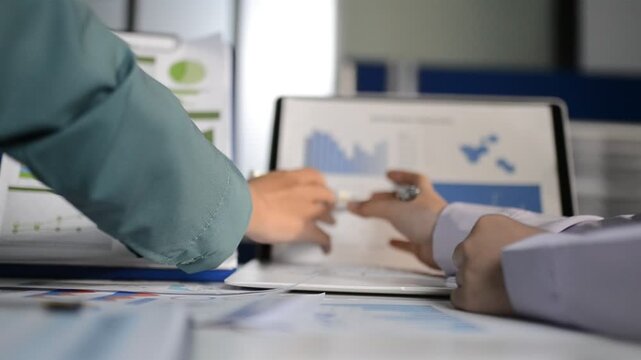 Close up of two asian colleagues working together, have a disussion and using laptop computer at office with financial document on desk