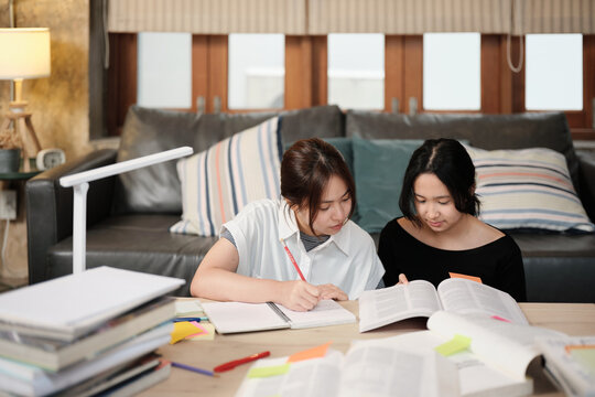 Two Asian teenage girls learning tutorials at home together, reading textbooks, writing notes, self-tutorial exams, preparation for back to school, Homeschooling study, knowledge education lifestyle.
