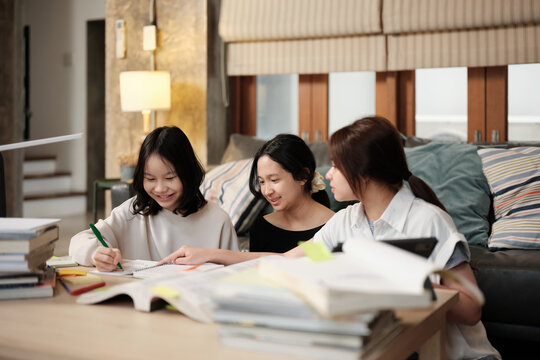 Three Asian teenage girls learning tutorials at home together, reading textbooks, writing notes, self-tutorial exams, preparing school homework, Homeschooling study, knowledge education lifestyle.