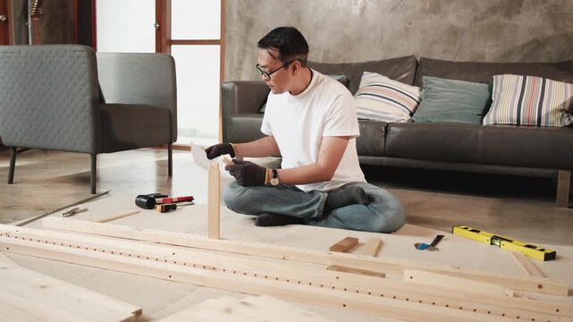 Asian mature man self-assembling flat-pack furniture with DIY tools and instruction guide, confused with wooden parts, home improvement, craft installation, hobby workshop, handyman active lifestyle.