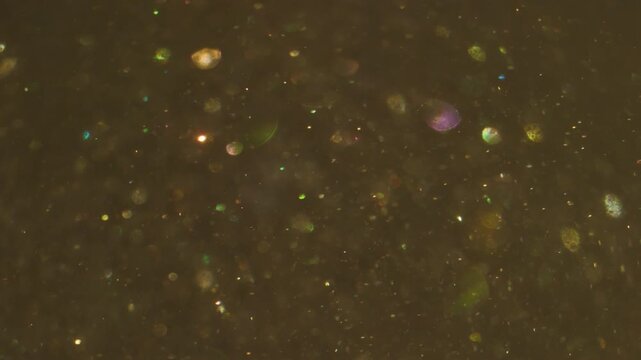 Defocused twinkle particles. Glitter light. Yellow sparks spiral stream on dark abstract background. Color flicker dots blur texture.