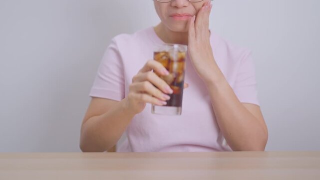 Woman drinking carbonated ice water and feeling sensitive teeth to cold pain, hand holding glass of cold sparkling water. dental health problem from soda acidity, toothache and oral care concept