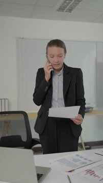 Angry businesswoman talking on smartphone while checking documents