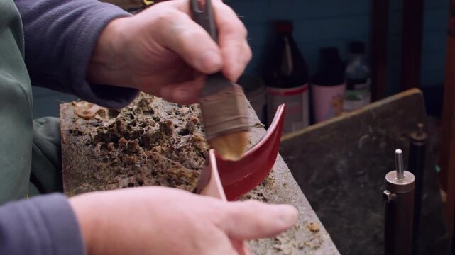Master occupation. Footwear manufacturing. Unrecognizable man professional cobbler hands applying glue for shoe sole using brush in workshop.