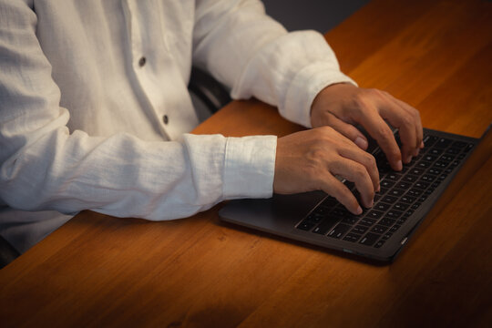Close up view of freelance male hands typing on laptop computer keyboard while working at wooden office desk using internet technology for digital communication and work.