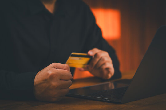 Angry man holding credit card with clenched fist at laptop. This financial stress concept shows frustration from debt, online shopping fraud, scam, or a declined payment.