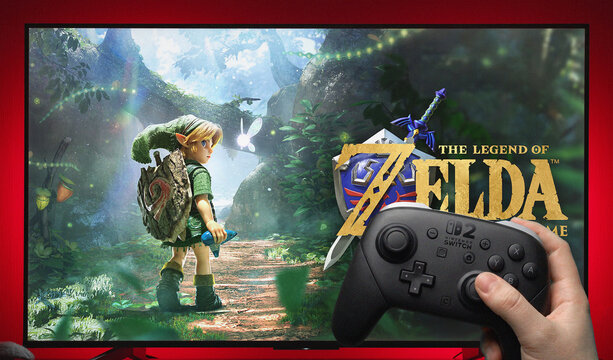 Person Holding Nintendo Switch 2 Controller in Front of TV Screen Displaying the Legend of Zelda Ocarina of Time Game Title