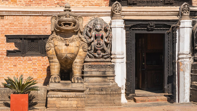 Stone sculpture of a lion at the entrance to the building. Mouth open, big teeth. Beautiful carvings. On the wall is a bas-relief depicting a four-armed god Hanuman. Nepal. Kathmandu. Durbar Square.