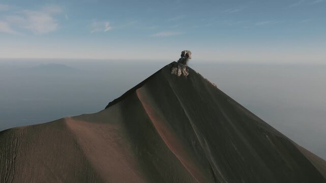 Drone shot of Volcan de Fuego erupting at dawn, seen from Acatenango hike. Dramatic plume of dark ash rises from volcanic peak, crisp morning light, wide landscape view.