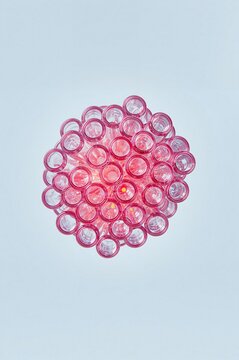 A circular cluster of many small pink glass test tubes arranged in a honeycomb pattern against a light blue background, with soft glowing, light inside
