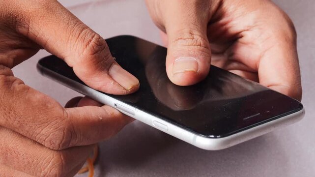 Close-up of Asian man's hands securing a slightly lifted smartphone screen with a rubber band as a temporary repair. Phone maintenance, financial hardship, and extending device use.
