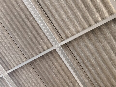 Close-up underside view of weathered gray corrugated fiber cement roofing panels secured by a silver metal frame grid