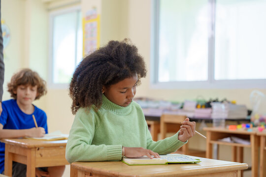 Young African American schoolgirl focusing on her book and writing during a lesson in a bright elementary school classroom