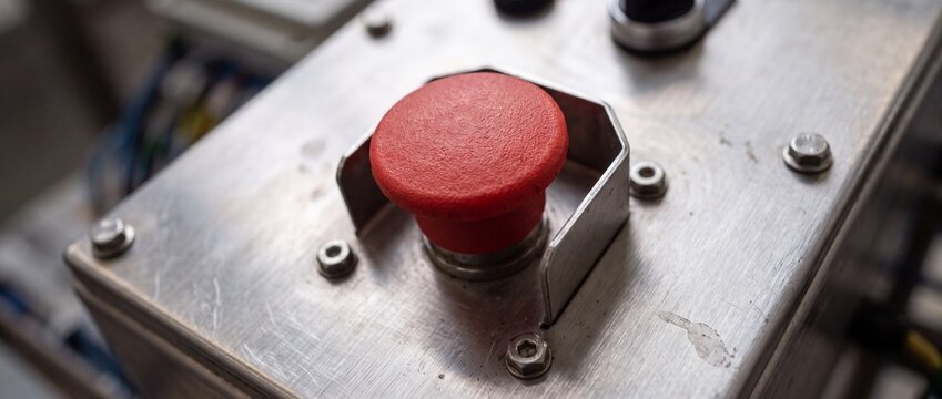 Industrial red emergency stop button on brushed metal panel offers critical safety function for machinery and equipment operation