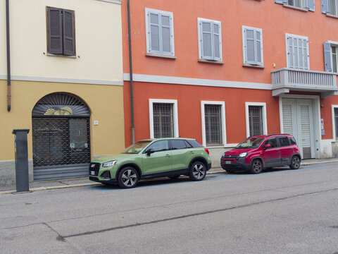 A green Audi Q2 and a red Fiat Panda are parked side-by-side on a street in front of a yellow and orange building