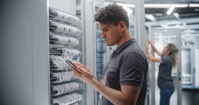 Network Engineer Examines Equipment Connections and Verifies Technical Information on Site, While Female Colleague Maintains Another Cabinet Nearby. Concept of Routine Work in Modern Server Facility.