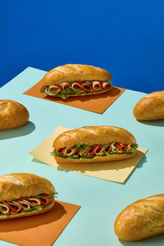 Several Vietnamese banh mi sandwiches arranged among individual baguettes on paper sheets, creating a playful food spread with repeated product forms.