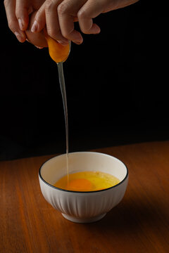 Close up hands cracking fresh raw egg with liquid egg white dripping down into white bowl.