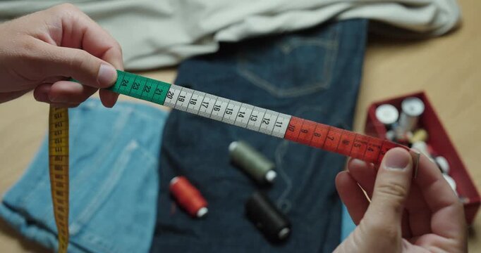 Close-up of hands holding and checking a colorful measuring tape while preparing for sewing and tailoring clothes at home.
