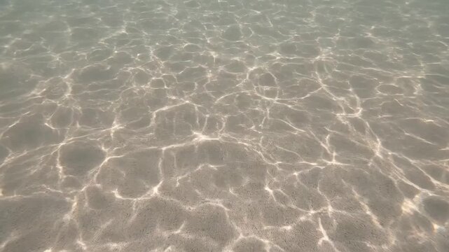 Sunlight patterns shimmering on sandy ocean floor underwater