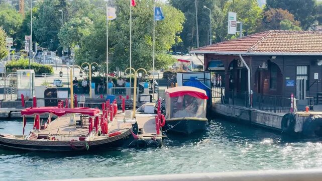 ISTANBUL, TURKEY - AUGUST 14, 2026: Traditional Ottoman style excursion boats moored at Eyup Sultan pier with local people walking on waterfront promenade during sunny day on Golden Horn bay.