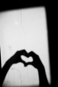 Close up black and white shadow of heart shape hand gesture on the dirty wall