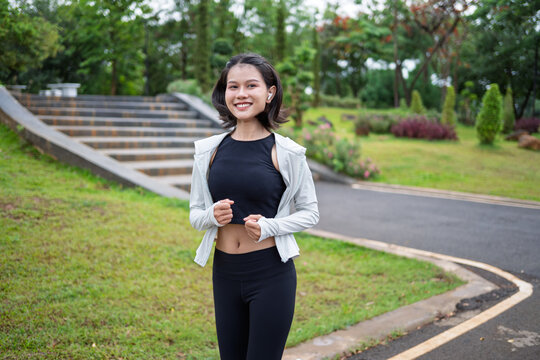 Asian Gen Z woman jogging in green urban park for wellness fitness and active city lifestyle