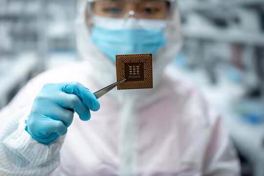Clean room technician in protective clothing holds a computer chip with tweezers in a modern electronics laboratory.