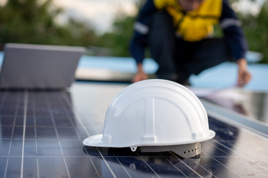 White safety helmet resting on solar panels while a worker reviews plans in the background, showing renewable energy installation and workplace safety.