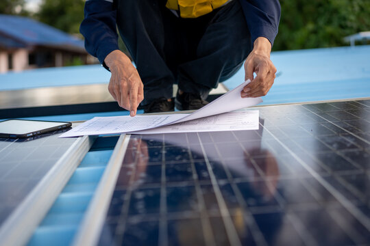 Solar energy technician reviews paperwork beside rooftop solar panels, checking installation details during an outdoor renewable power project.
