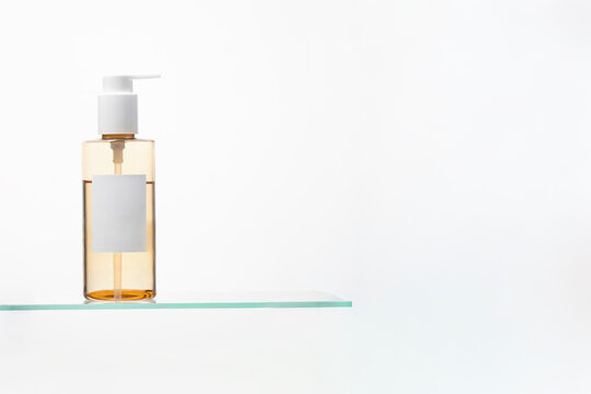 Pump bottle filled with golden oil liquid on glass shelf. Minimalist spa and beauty concept for luxury skin cleansing.Copy space
