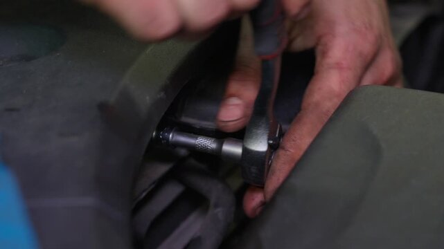 Technician secures metal fastener on blue and black outdoor equipment using hand tool during detailed maintenance. Craftsperson checks strap alignment and applies controlled pressure during repair.