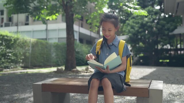 Asian girl reading book on school campus bench