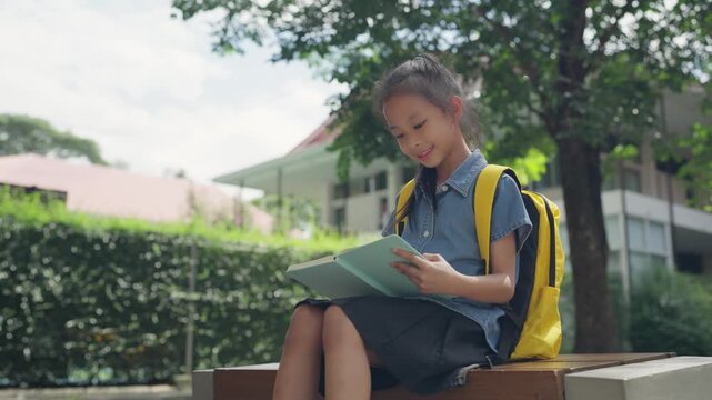 Asian girl reading a book on a bench outside school