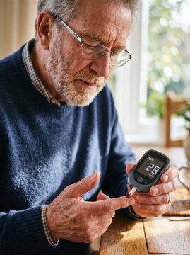 Elderly man checking blood coagulation level with portable INR meter at home