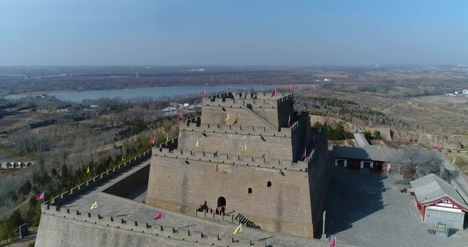 Aerial drone view of Zhenbei Tower in Yulin, historic Ming Dynasty fortress on the Great Wall with red and yellow flags, overlooking river and flatlands