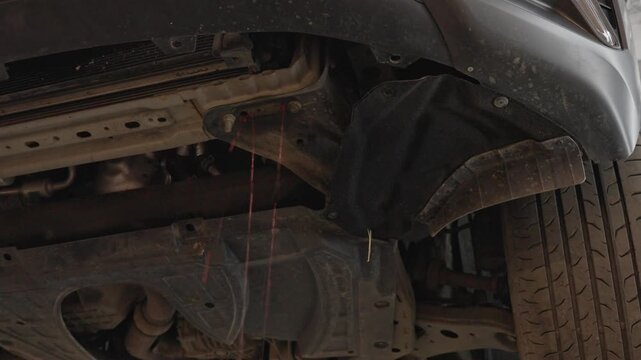 Car undercarriage drips water after road driving, with dirty tire and wheel well in gritty industrial style close view. Vehicle underside shows wet grime, mud, and suspension details.