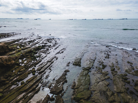 Rocky coastal shoreline in Ballenita, Ecuador, with waves washing over natural rock formations and tide pools beneath a bright sky over the Pacific Ocean.