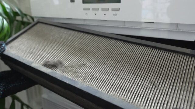 Air filter replacement. A person wearing gloves removes a dirty filter from the air purification system. An old, dirty air filter.