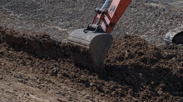 Heavy excavator lowers hydraulic bucket into rough soil and opens narrow trench for ground preparation. Tracked earthmover shifts loose earth while excavation line extends forward.