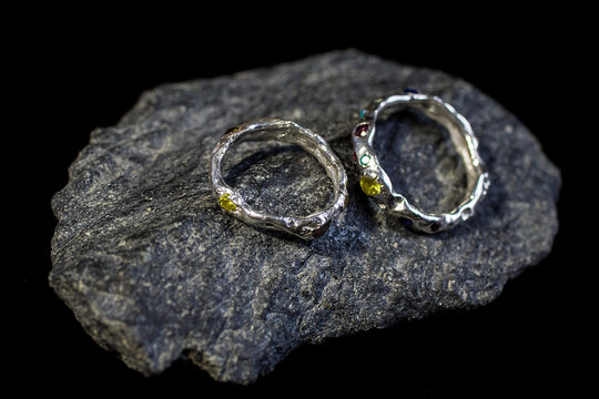 Two unique silver rings with a textured design and yellow gemstones, placed on a dark stone surface. Ideal for showcasing handmade jewelry.