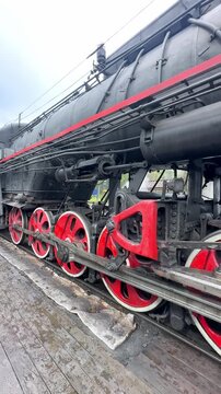 Karelia, Russia. Ruskeala Express. Vintage steam locomotive with a prominent red star emblem stands on the tracks at a railway station, releasing steam into the air. Vertical footage 