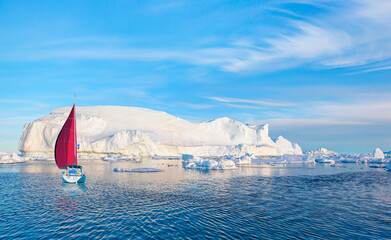 Giant iceberg near Kulusuk with lone yacht with red sails - Greenland, East Greenland © muratart