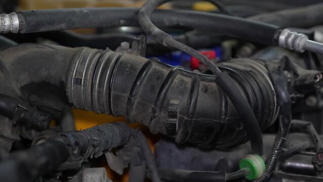 A black rubber air intake hose is prominently featured amid the complex system of tubes and wires inside a car engine bay.