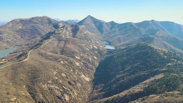Aerial view of ancient stone wall winding across rugged mountain ridges in Qifeng Mountain, Henan, with reservoirs and sparse winter vegetation