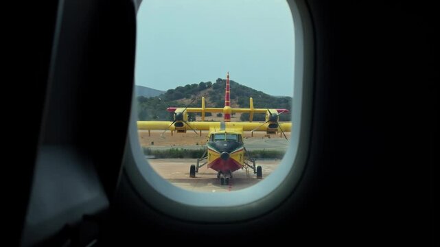 Point of view from an airplane window looking at a yellow firefighting canadair cl-415 aircraft parked on the airport runway in olbia