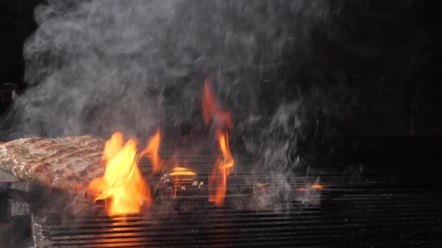 Chef spatula flipping juicy beef patty on hot grill. Intense orange flames and thick smoke rising, professional restaurant kitchen, delicious burger cooking process Slow motion 4k video