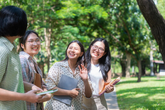 Group of happy asian female university students talking and laughing together in a park, smiling college friends holding books and having a friendly conversation outdoors on campus