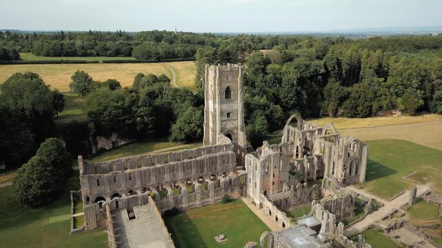 Ancient stone ruins stand tall amid verdant fields. Sunlight glows warmly over weathered towers and archways. Fountains Abby, World Heritage Site near Harrogate North Yorkshire UK,