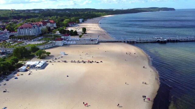 The seaside promenade and sandy beach in Sopot, Poland, come into view as the drone flies forward, with the long pier and Baltic Sea in the background.